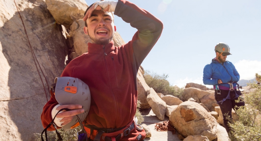 two students in rock climbing gear stand amongst rocks and green shrubs